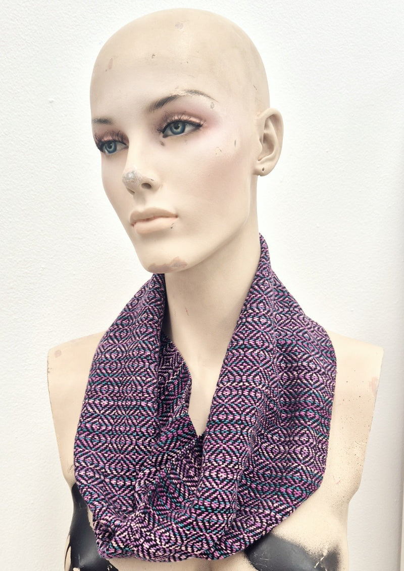 Creepy mannequin wearing a handmade handwoven infinity loop scarf in various shades of pink, teal and black