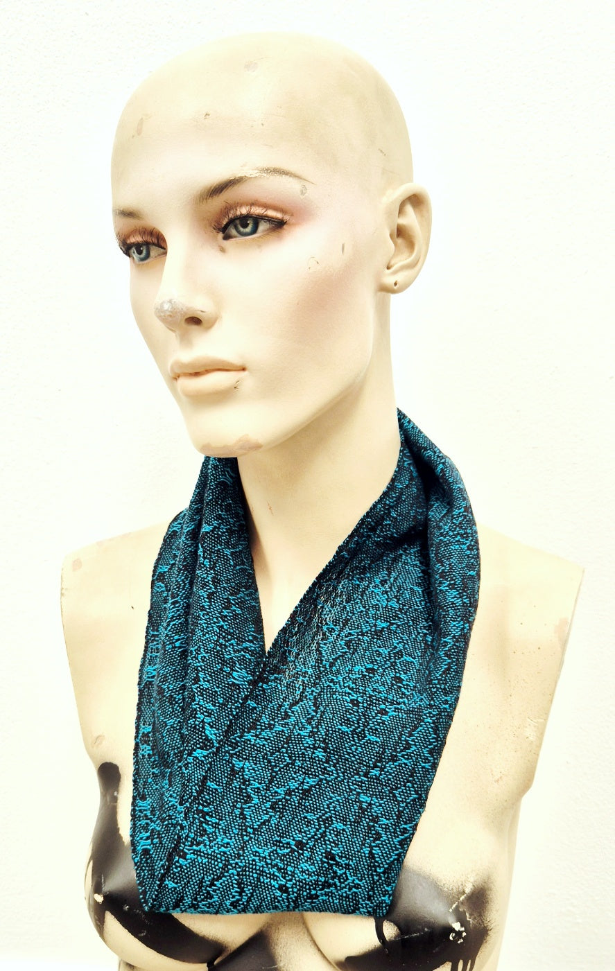 Mannequin wearing a turquoise blue handwoven patterned scarf on a white background