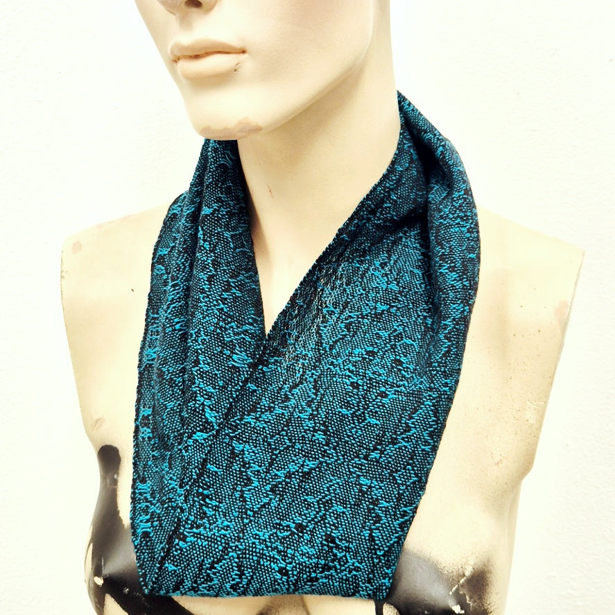 Mannequin wearing a turquoise blue handwoven patterned scarf on a white background