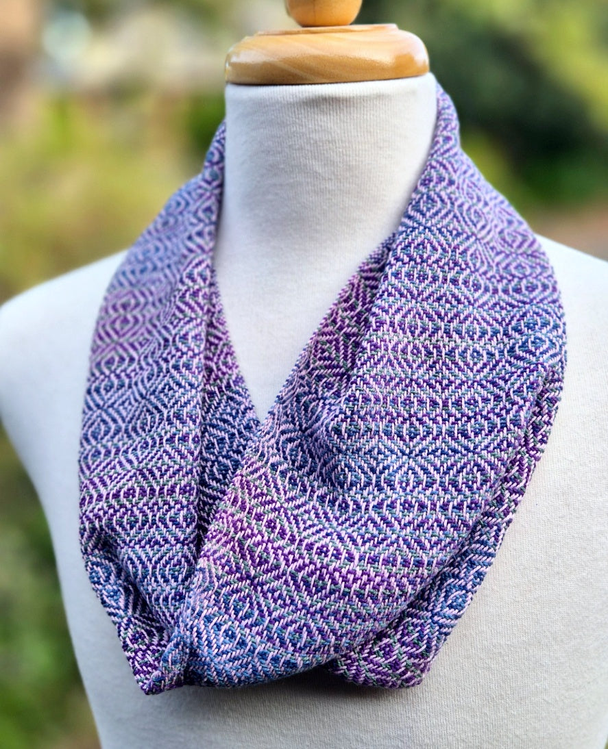 Purple, pink and blue patterned scarf on a mannequin against a blurred natural background