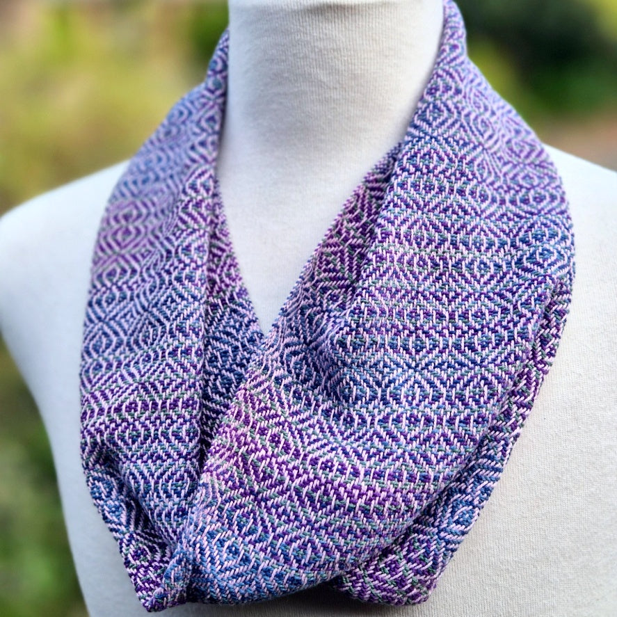 Purple, pink and blue patterned scarf on a mannequin against a blurred natural background