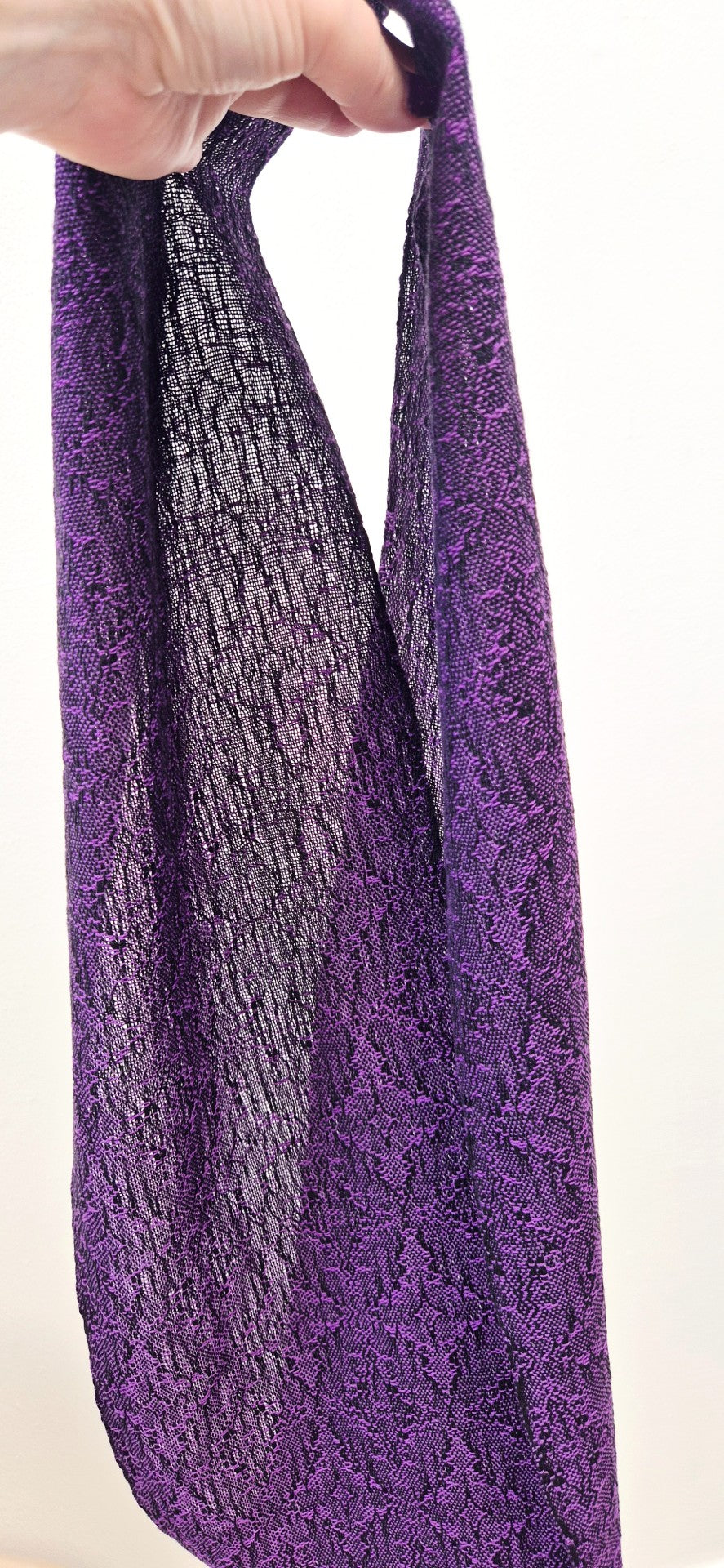 Purple fine textured fabric held by a hand against a white background