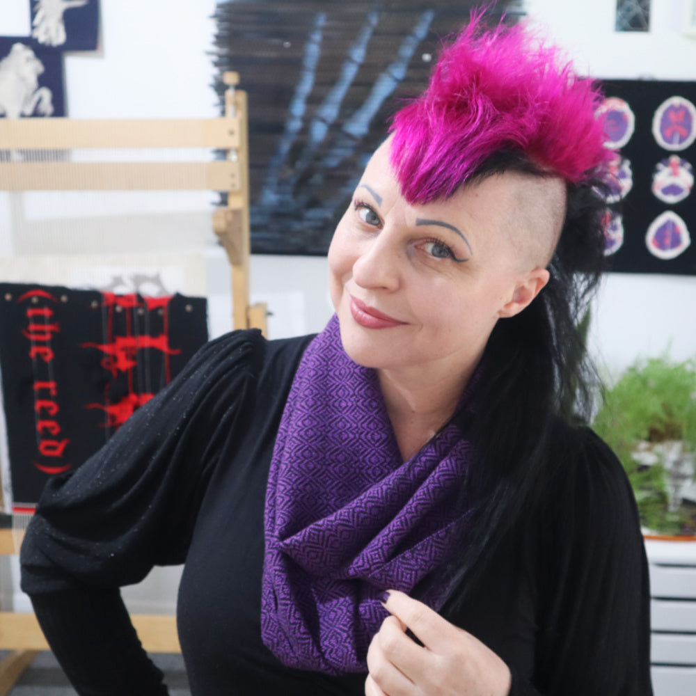 Person with pink mohawk hair and a purple handwoven scarf in an indoor setting