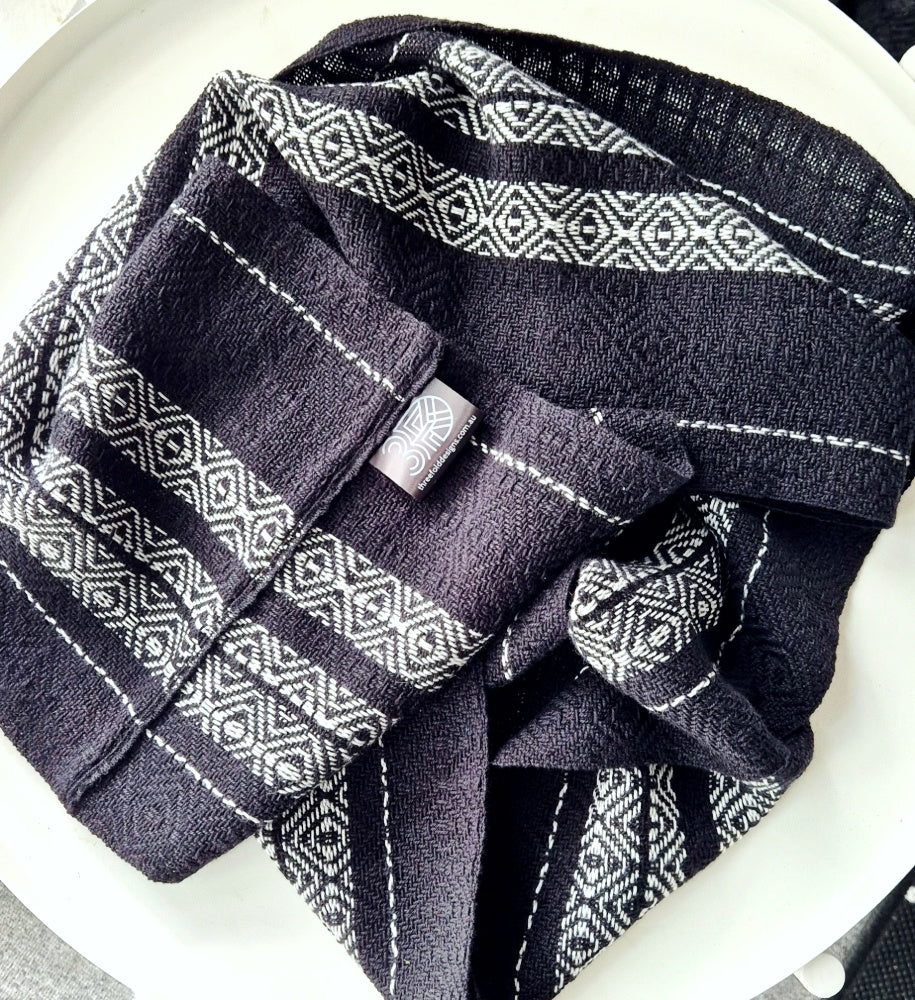 Folded black and silver grey patterned handwoven scarf on a white surface