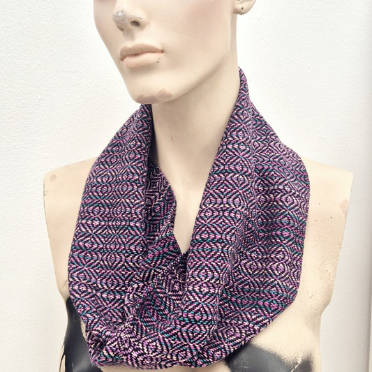 Creepy mannequin wearing a handmade handwoven infinity loop scarf in various shades of pink, teal and black