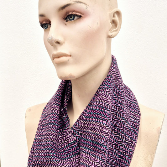 Handwoven infinity scarf in various shades of pinks, teals, and black, worn by a creepy mannequin
