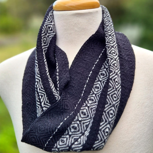 Black scarf with light grey geometric pattern on a mannequin against a blurred green background